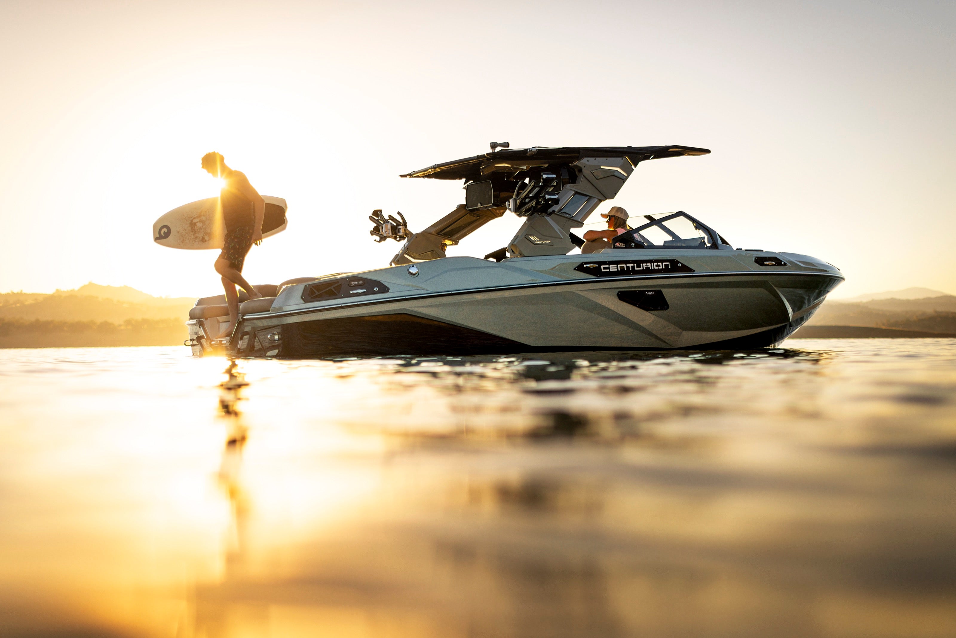 2027 Centurion RS245 at golden hour with a wakesurfer carrying a board across the swim platform